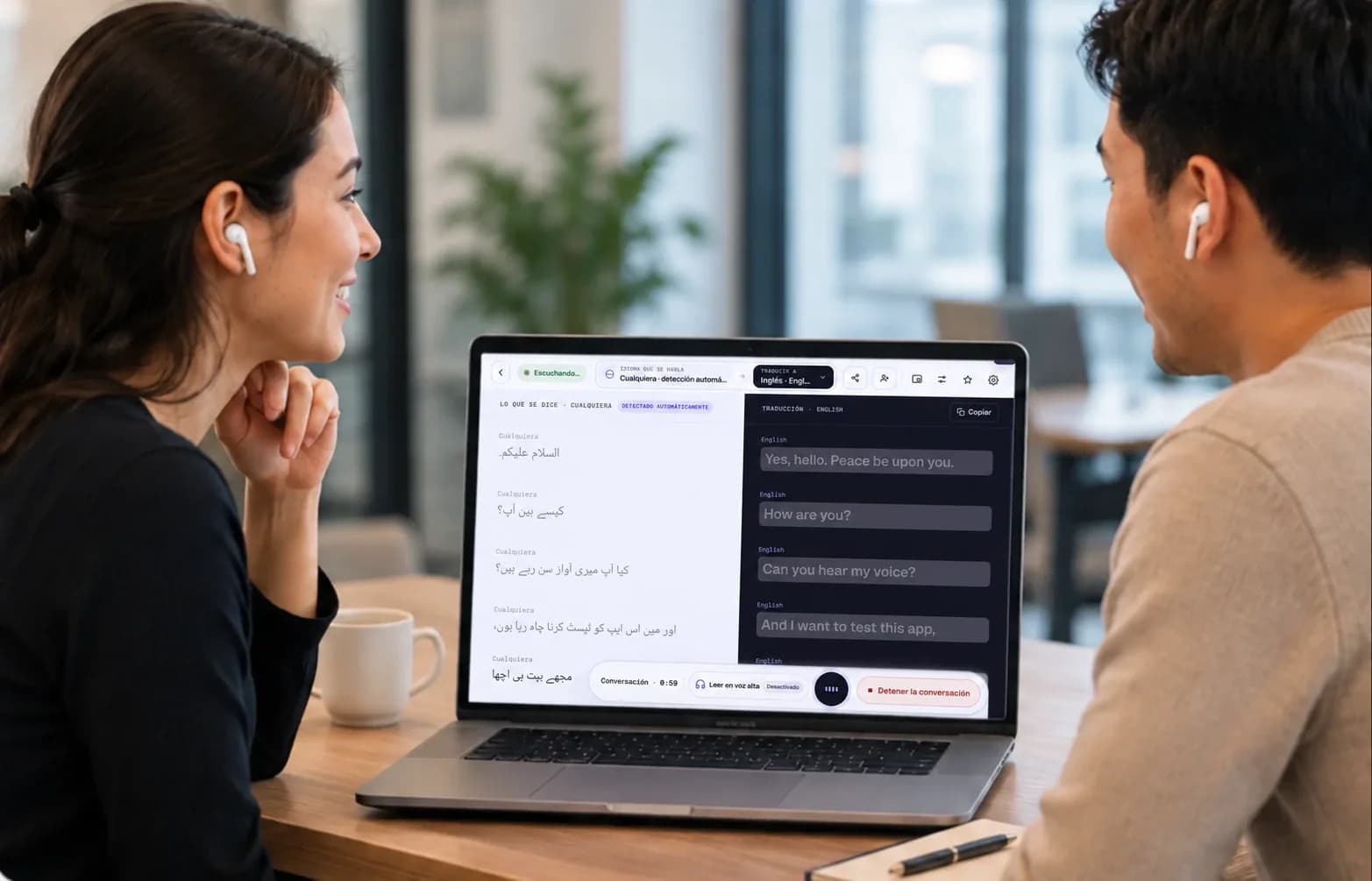Two people talking across an office table, each with their own earbuds in, while Mingle on the laptop between them translates their conversation live.